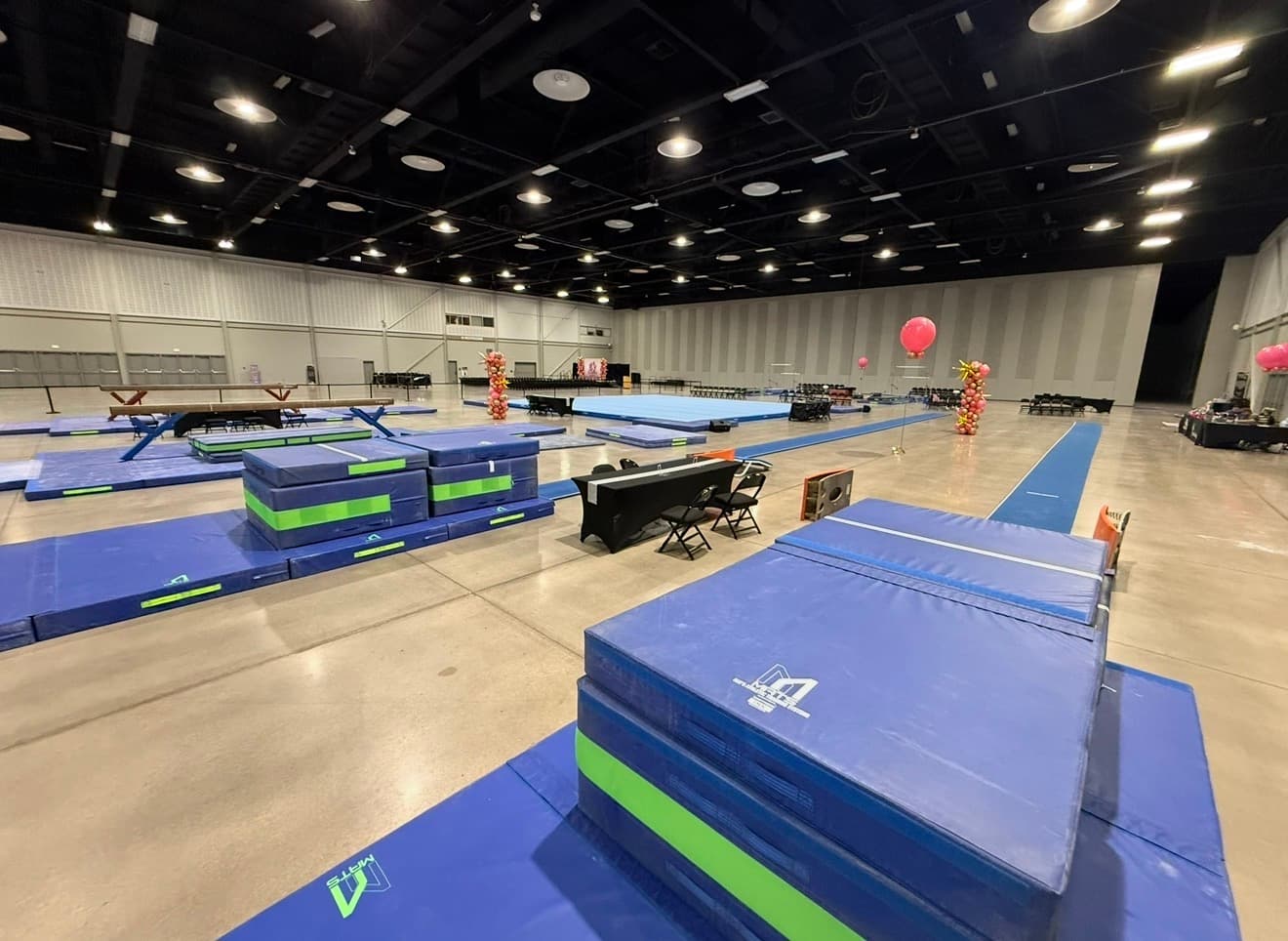 Vault runway, mats, and landing stacks set on a convention center floor ahead of a gymnastics meet.